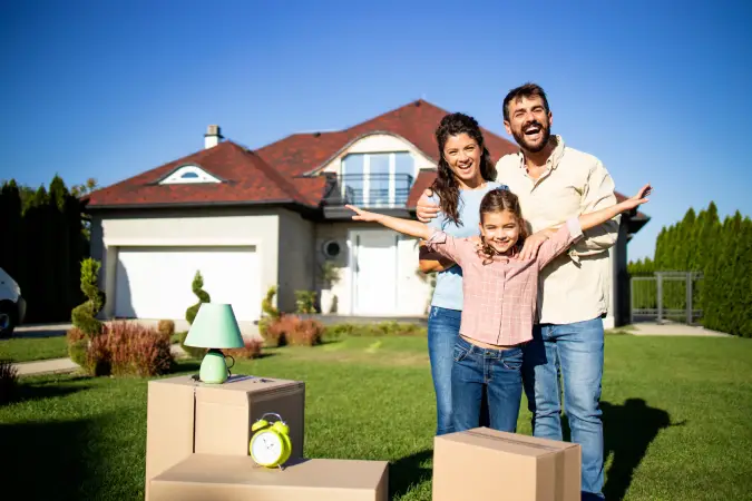 smiling 3-person family with moving boxes standing in front of the new house they bought that is covered with Vireya homeowners insurance