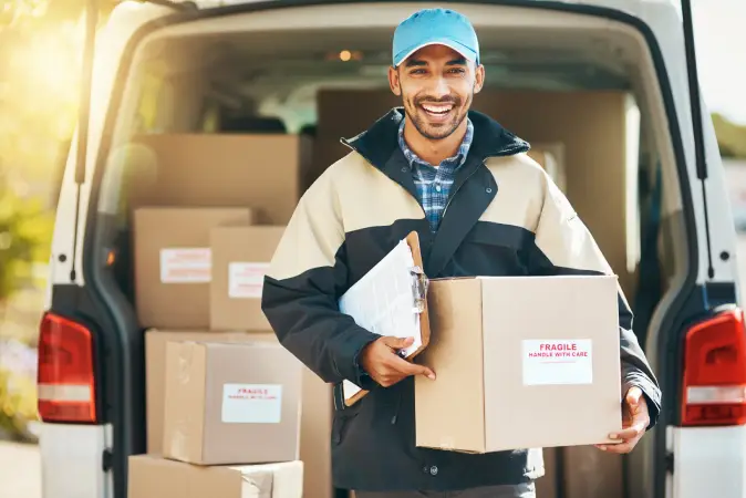 Smiling delivery man holding a box in front of a commercial vehicle full of other boxes