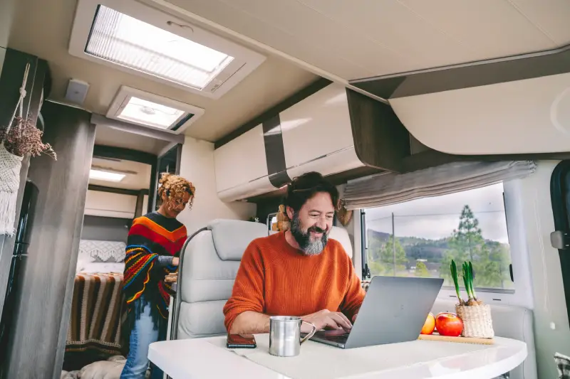 man sitting in RV with woman behind him as he searches and compares RV insurance rates on his laptop