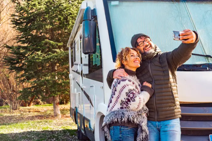 man and woman smiling and taking a selfie in front of the RV they've insured with Vireya