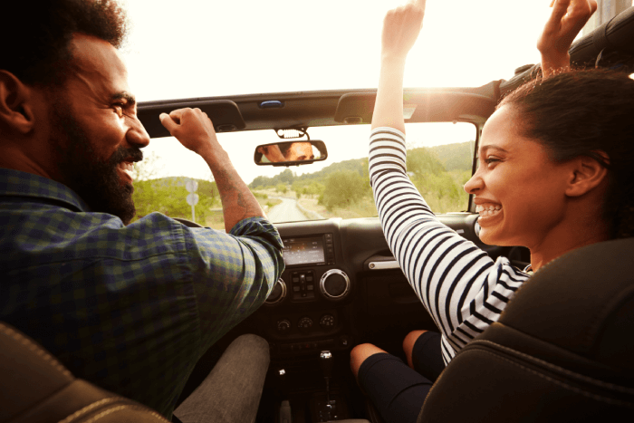 man and woman smiling in the front of seat of a convertible as they drive the down the road confidently knowing they're covered by auto insurance