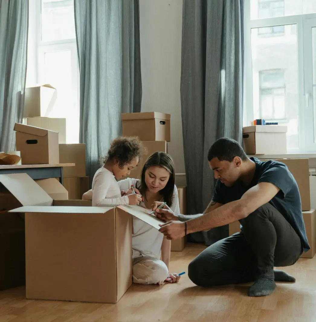 child inside a moving box with parents kneeling down next to her drawing on the box as they unpack in their new home covered by Vireya homeowners insurance