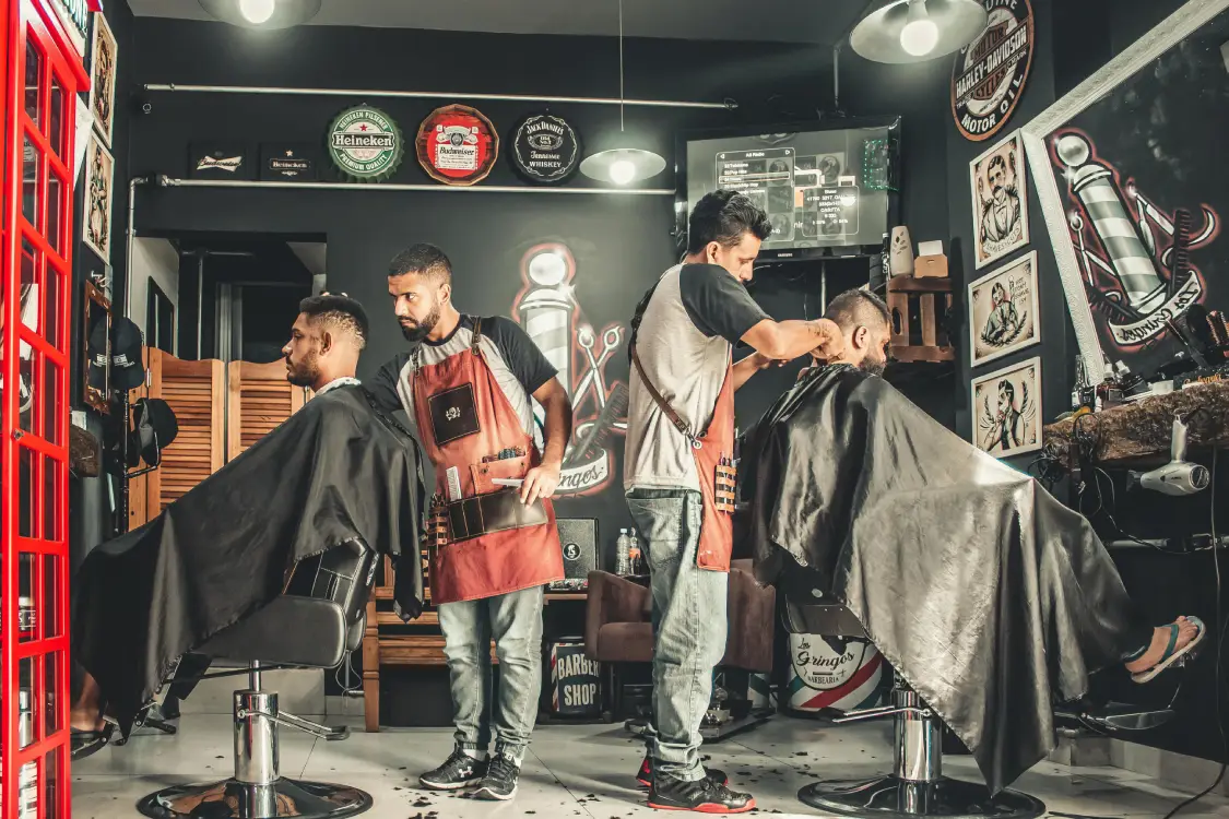 Two barbers cutting clients' hair in a stylish, modern barbershop covered by commercial insurance through Vireya