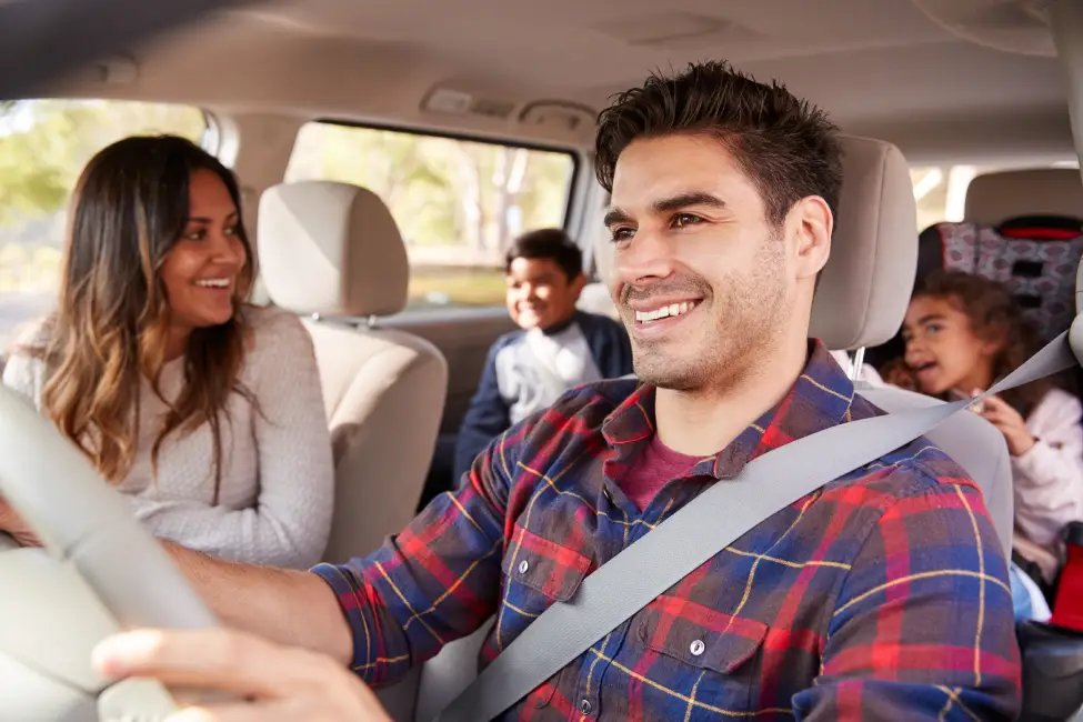 Smiling man driving his family of four in car protect with auto insurance from Vireya