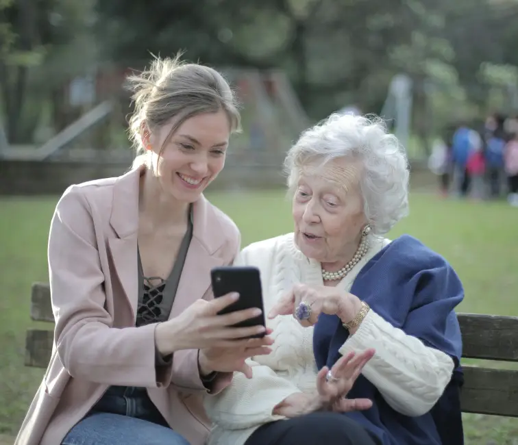 Young woman showing life insurance information on a smartphone to an elderly woman on a park bench