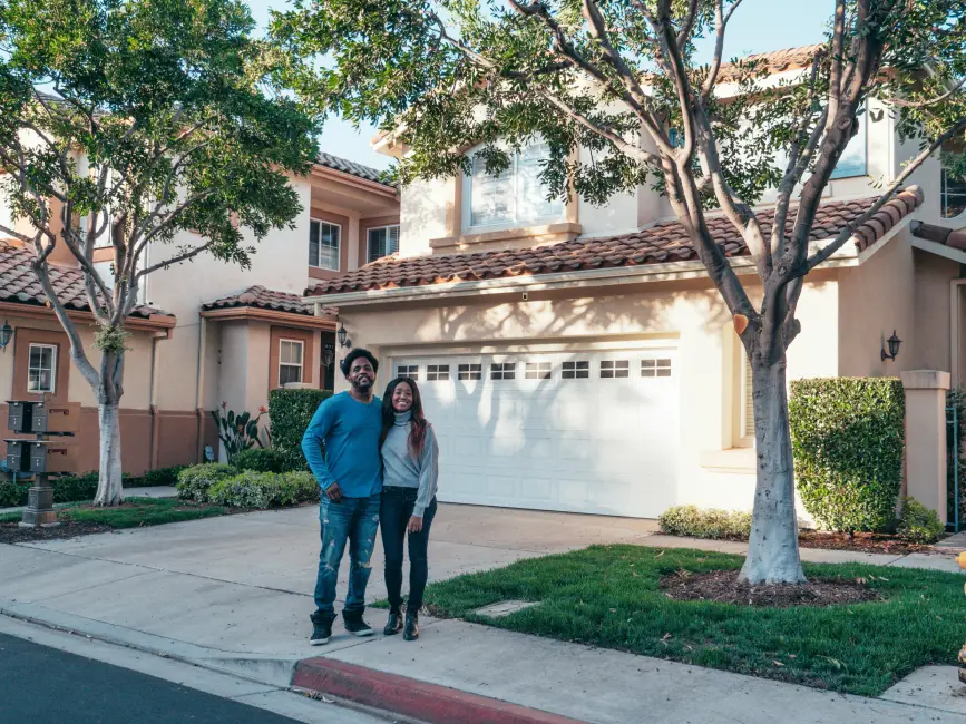 Smiling couple standing in front of a house that allows them to enjoy a homeowners discount on auto insurance