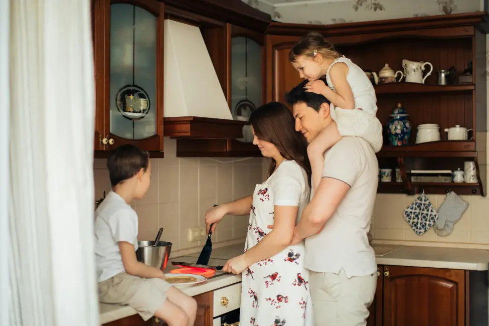 Happy family cooking together in a kitchen of the house protected by homeowners insurance, with a child on father's shoulders.