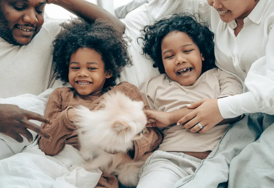 Two happy children and a pet, with parents, laughing and playing in bed